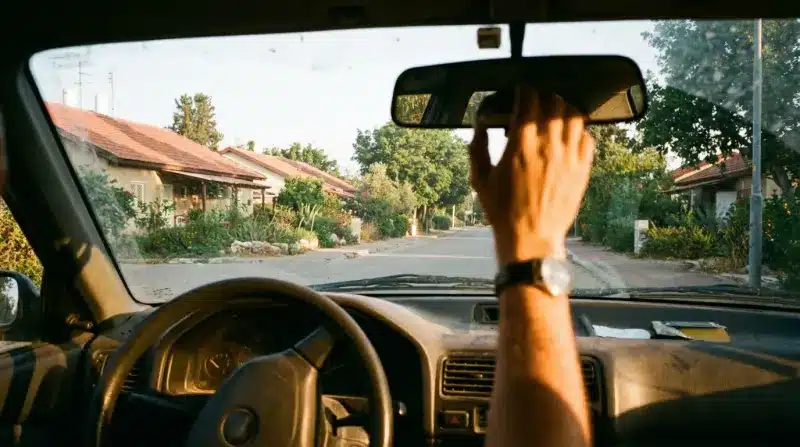 מבט ממושב הנהג ברכב: יד מכוונת את המראה האחורית, נסיעה בכביש שקט באור בין ערביים.