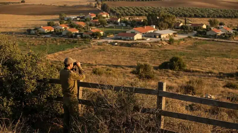 חייל צה"ל מבצע תצפית במשקפת לעבר יישוב כפרי באזור גבעות.