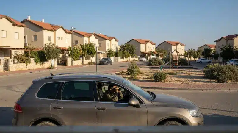 איש ברכב מביט במשקפת ברחוב של שכונת מגורים